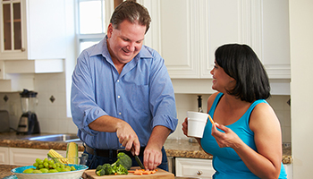A man cutting food alongside a woman with a mug