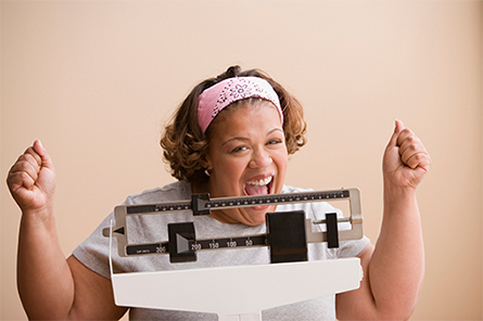A standing on a scale while smiling big at the camera