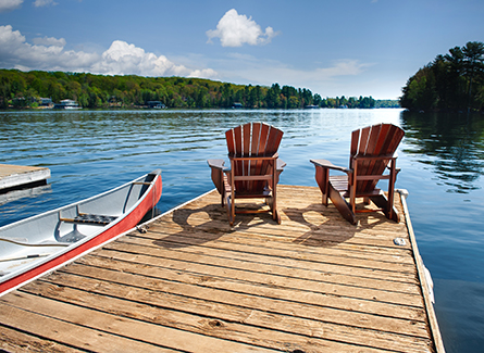 Adirondack chairs on a dock on a peaceful lake