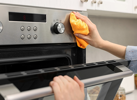 Photo of woman using orange rag to clean stove knobs