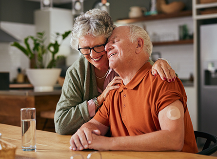 Senior couple hugging at kitchen table. Man is wearing continuous glucose monitor.