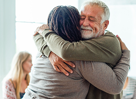 Elderly man and younger woman hugging in a support group
