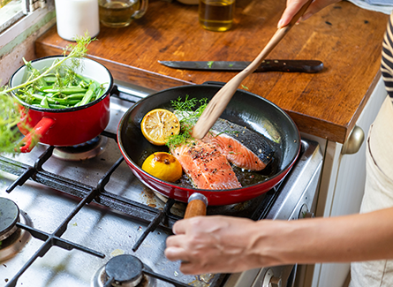Woman cooking salmon and vegetables on stove
