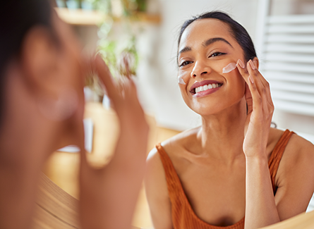 Woman applying sunscreen to her face in mirror