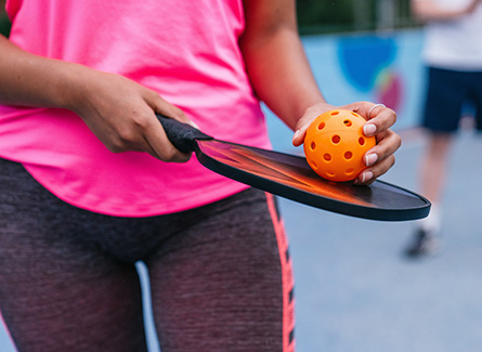 Woman in pink shirt holding pickleball paddle and orange ball
