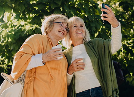 Two senior women taking a selfie while holding coffee