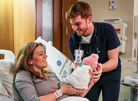Nurse handing baby to mother in maternity
