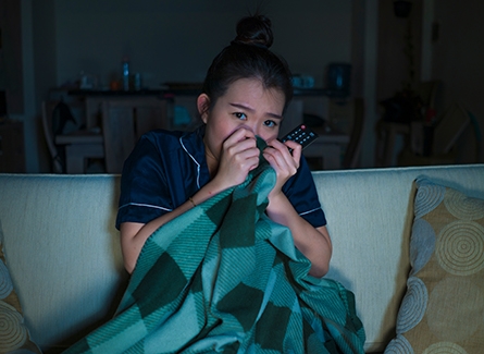 Woman watching a scary movie with blanket clutched in hands