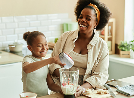 Woman laughing while making smoothie with daughter